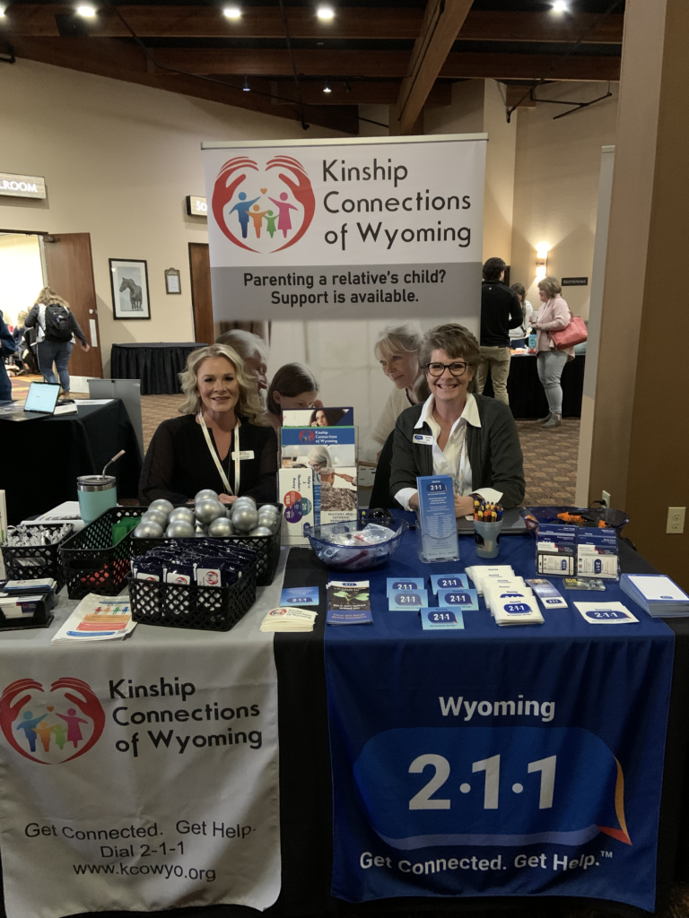 A Kinship Connections of Wyoming staff member and a Wyoming 2-1-1 staff member smile as they sit behind a table with information about their services