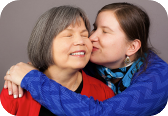 A Native elder closes her eyes as her daughter or granddaughter gives her a hug and a kiss on the cheek