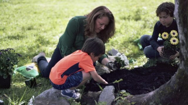 A Native woman gardens with two children