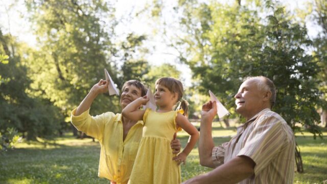 A white grandmother, grandfather, and young granddaughter prepare to throw paper airplanes outside together